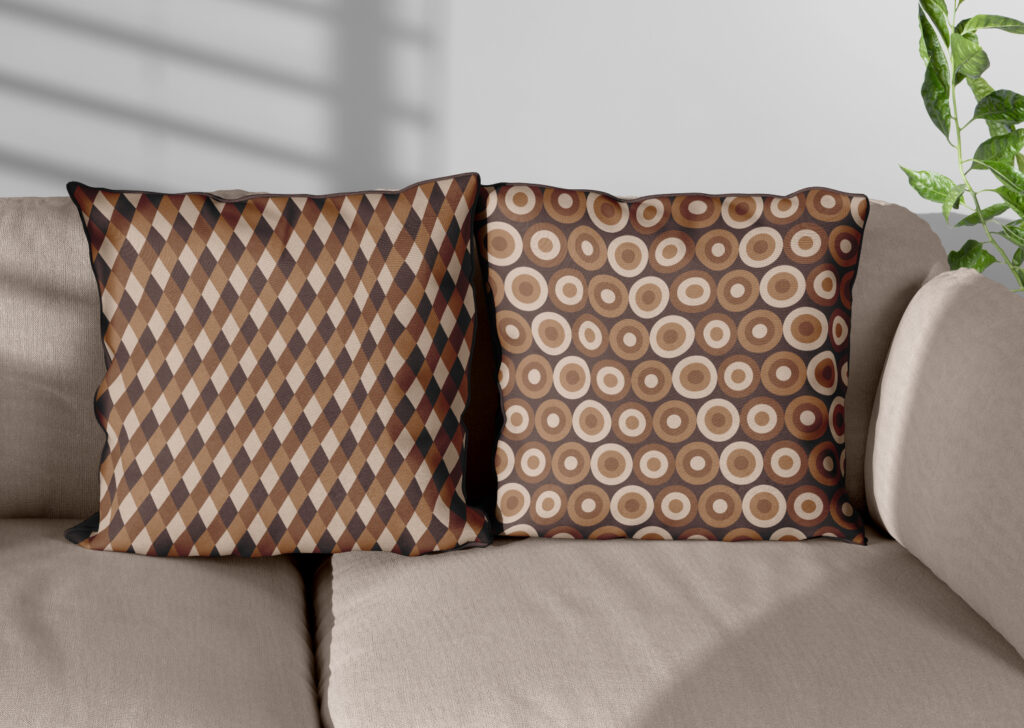 Tan sofa with two throw pillows. One has a design of thin brown diamonds alternating between four different shades. The other has a repeating pattern of concentric circles in three shades of brown against a background of very dark brown.